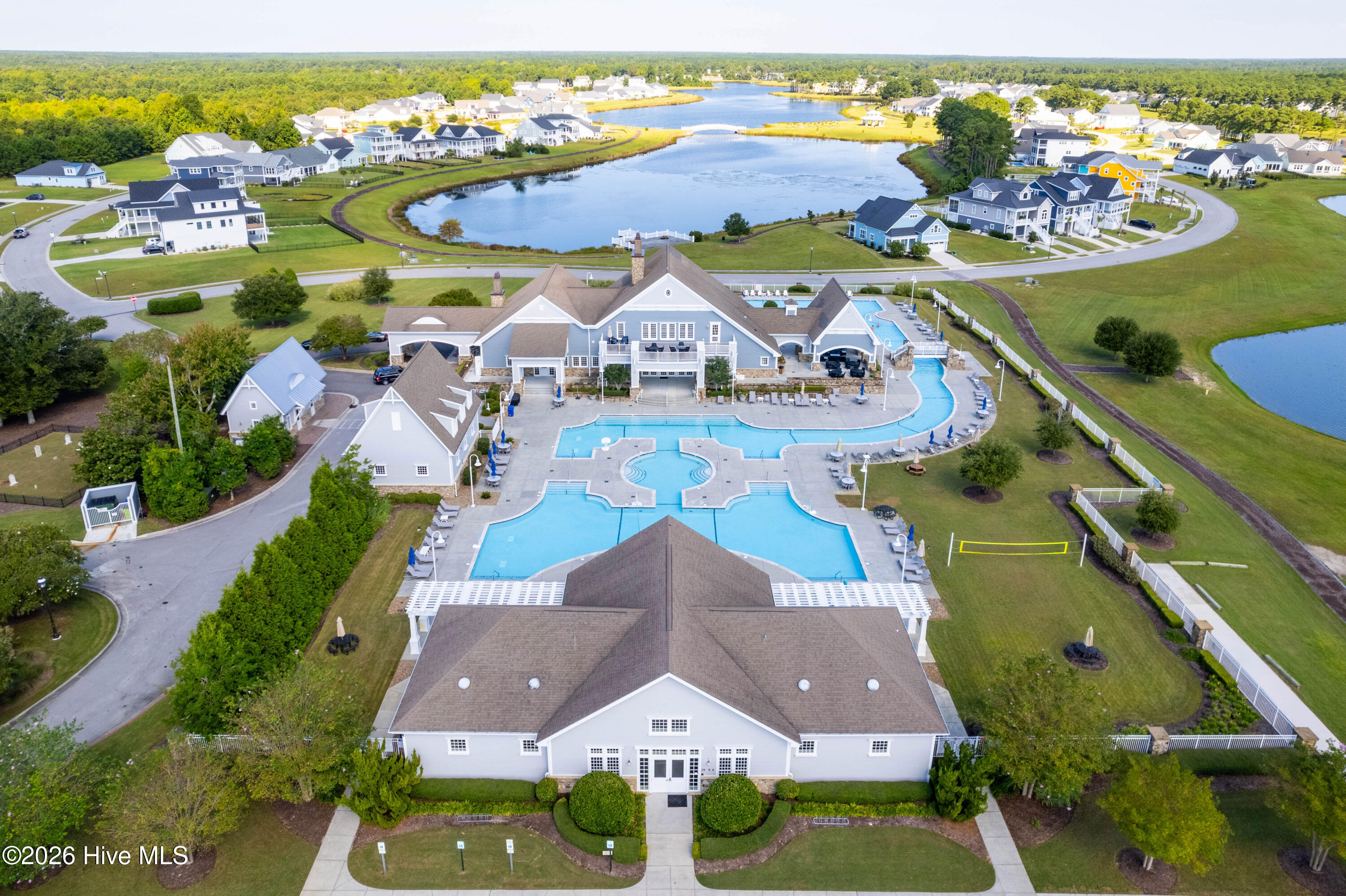 Aerial view of a community clubhouse with multiple pools beside lakes and surrounding homes.