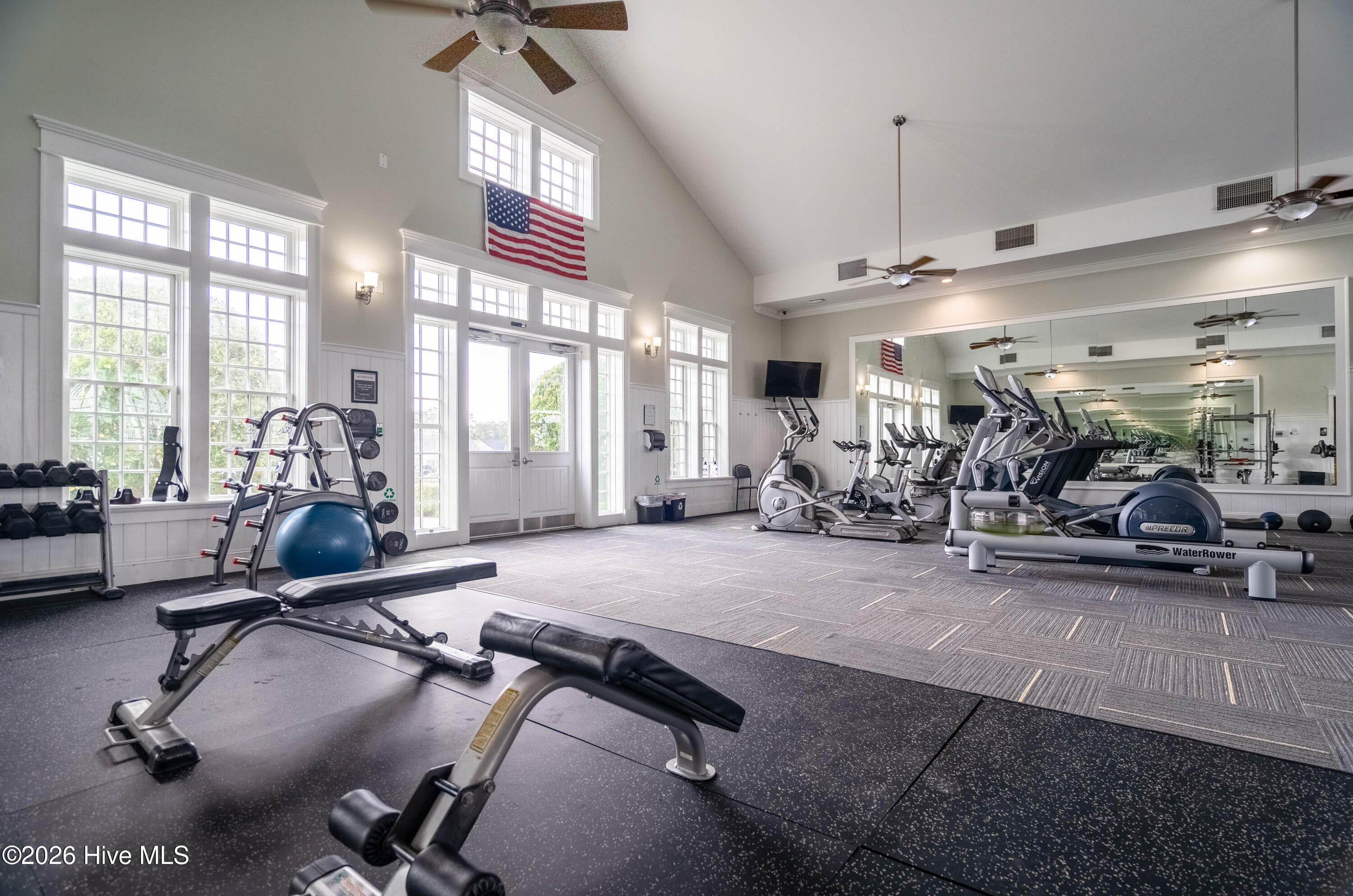 Bright fitness center with mirrored walls, large windows, and rows of exercise equipment.