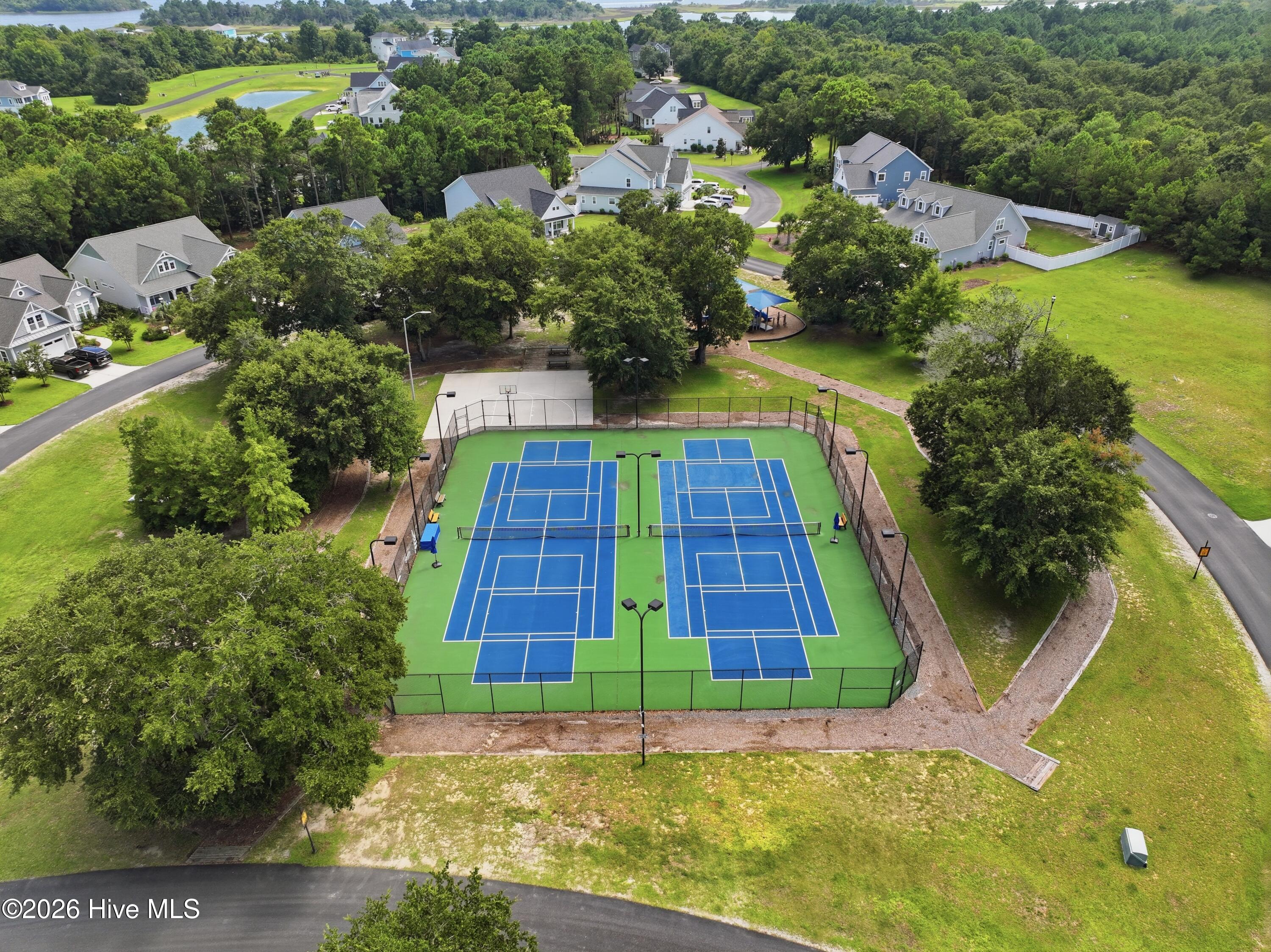 Aerial view of two blue tennis courts amid homes and trees.