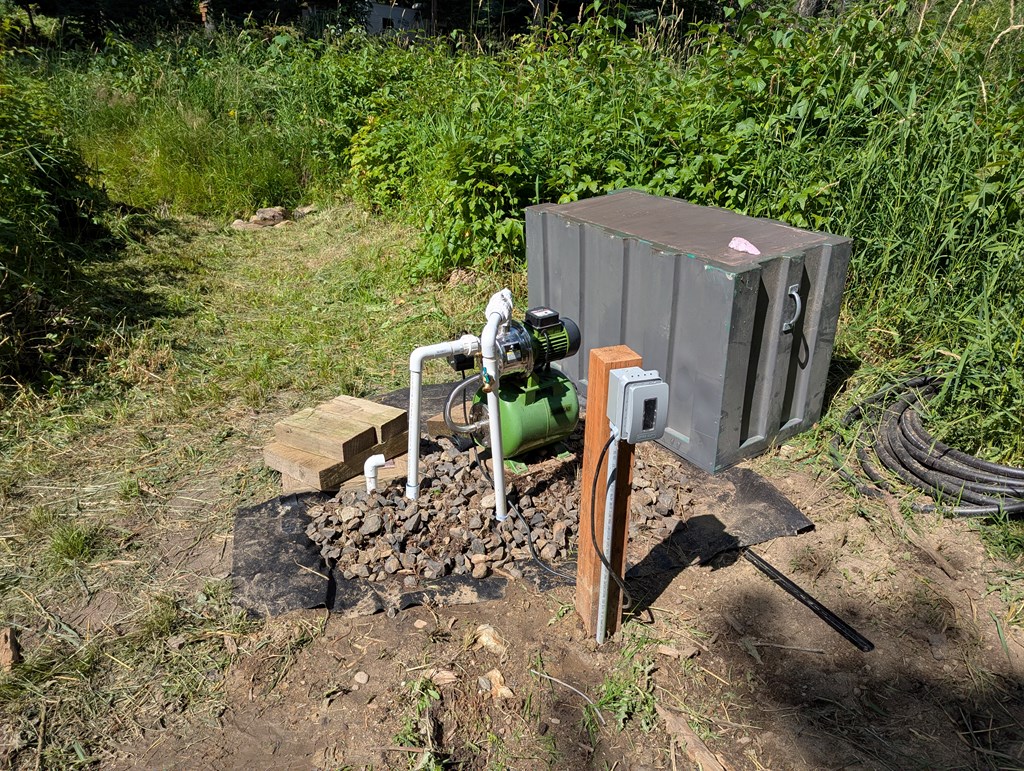 Well pump and utility equipment beside a cleared path on a wooded lot.