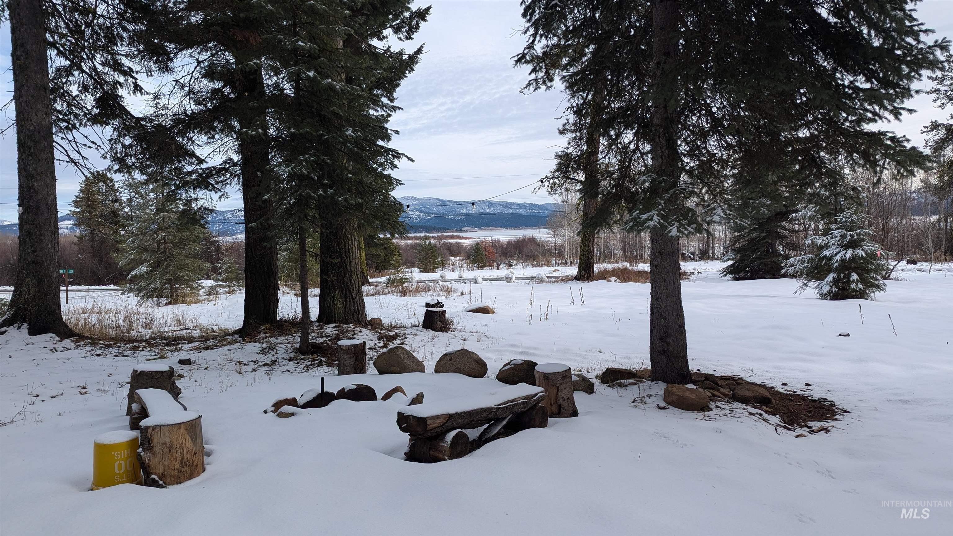 Snow-covered wooded property with a rustic log bench and distant mountain views.