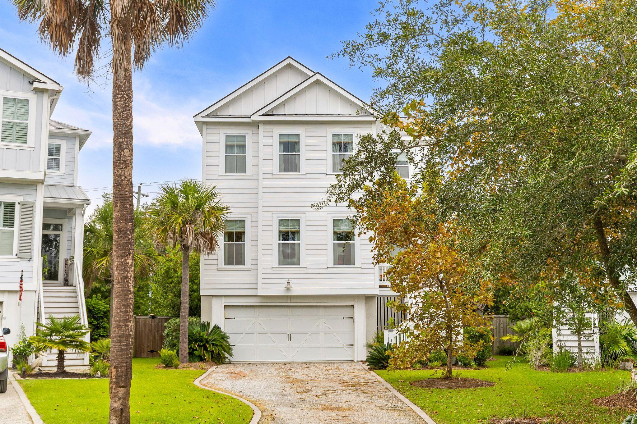 Two-story white house with a double garage, curved gravel driveway, lawn, and palm trees.
