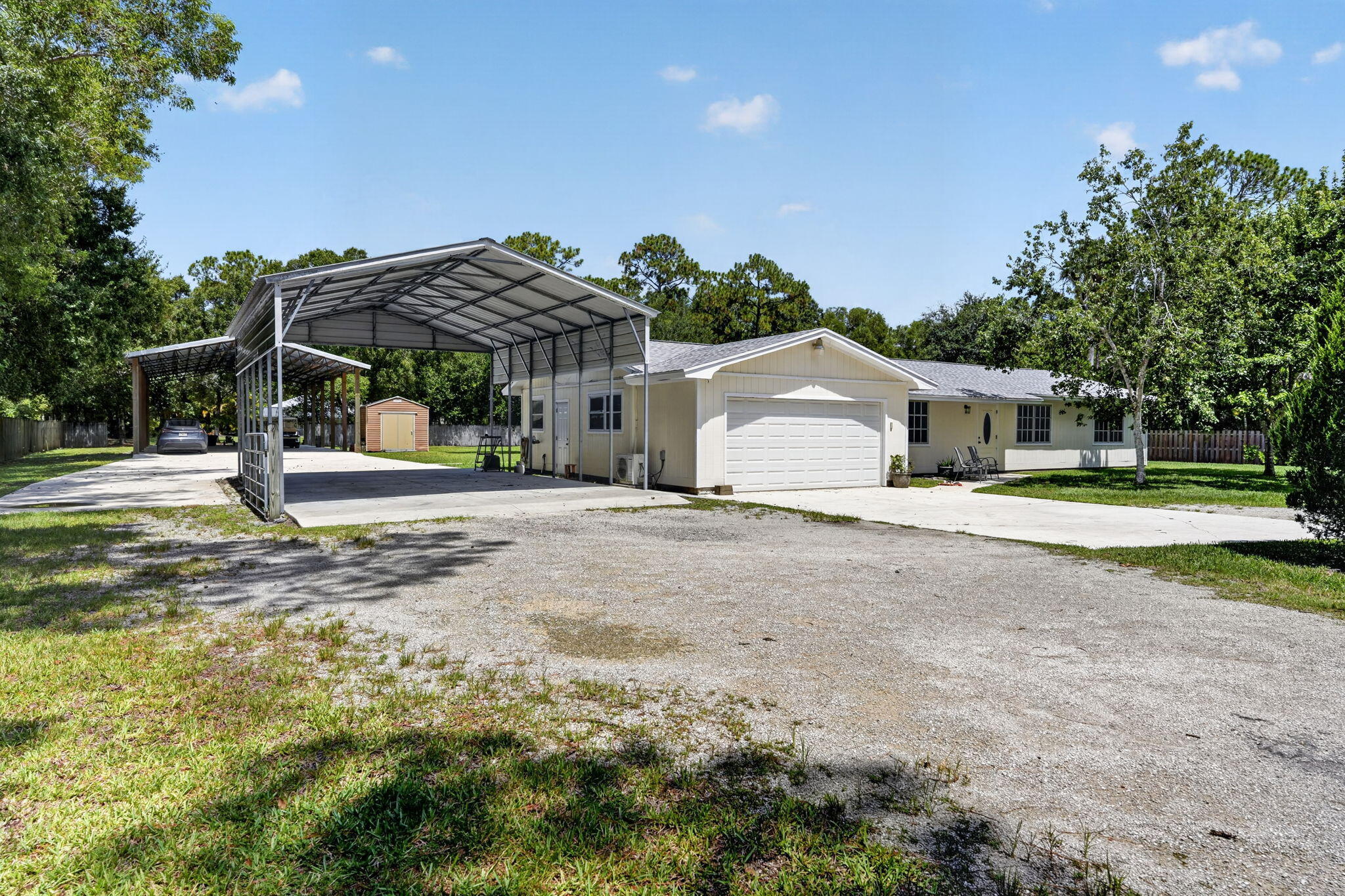 Single-story home with a two-car garage, large metal carport, gravel driveway, and small yard shed.