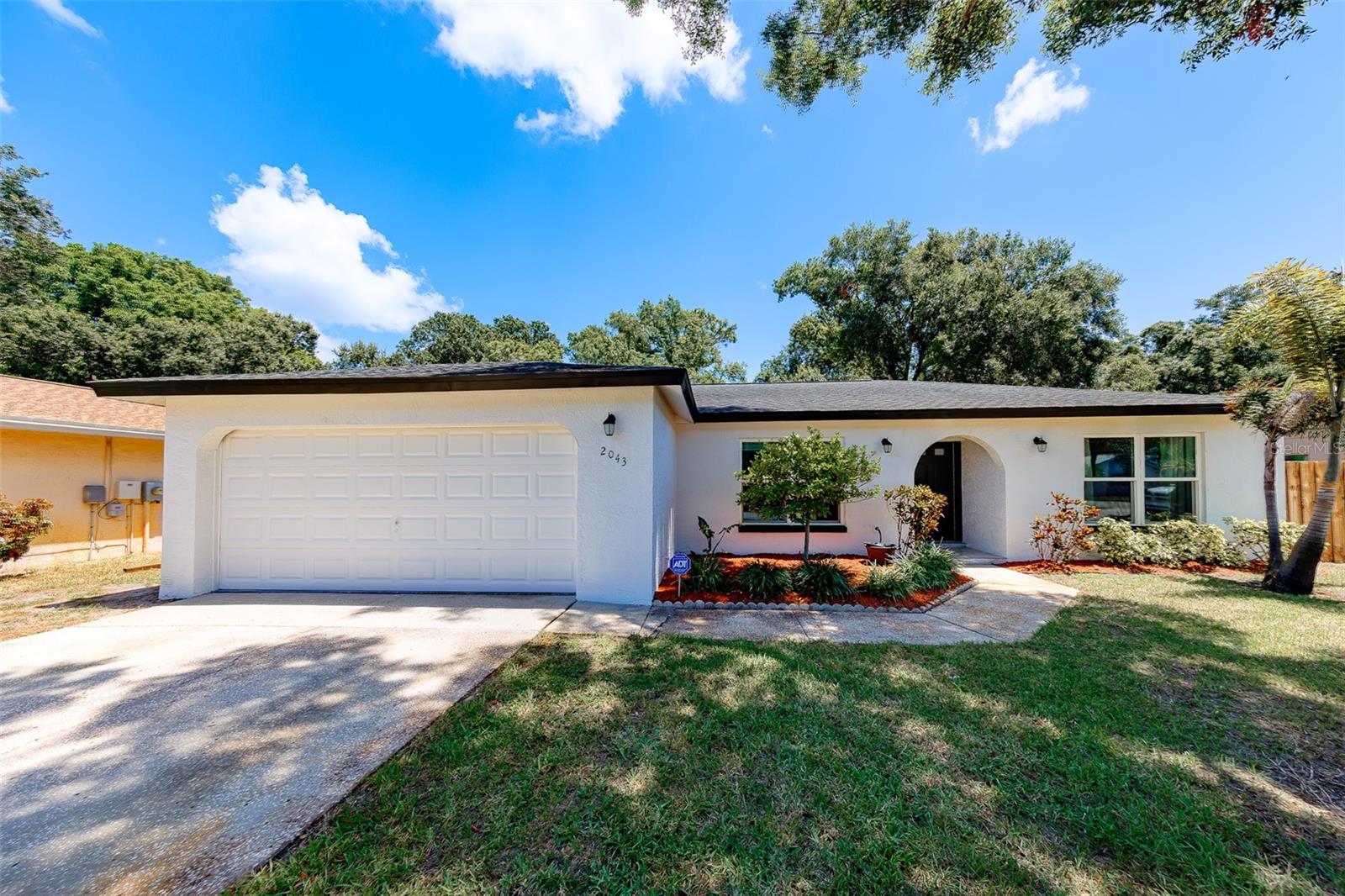 Single-story white stucco house with a two-car garage, arched entryway, and landscaped front yard.