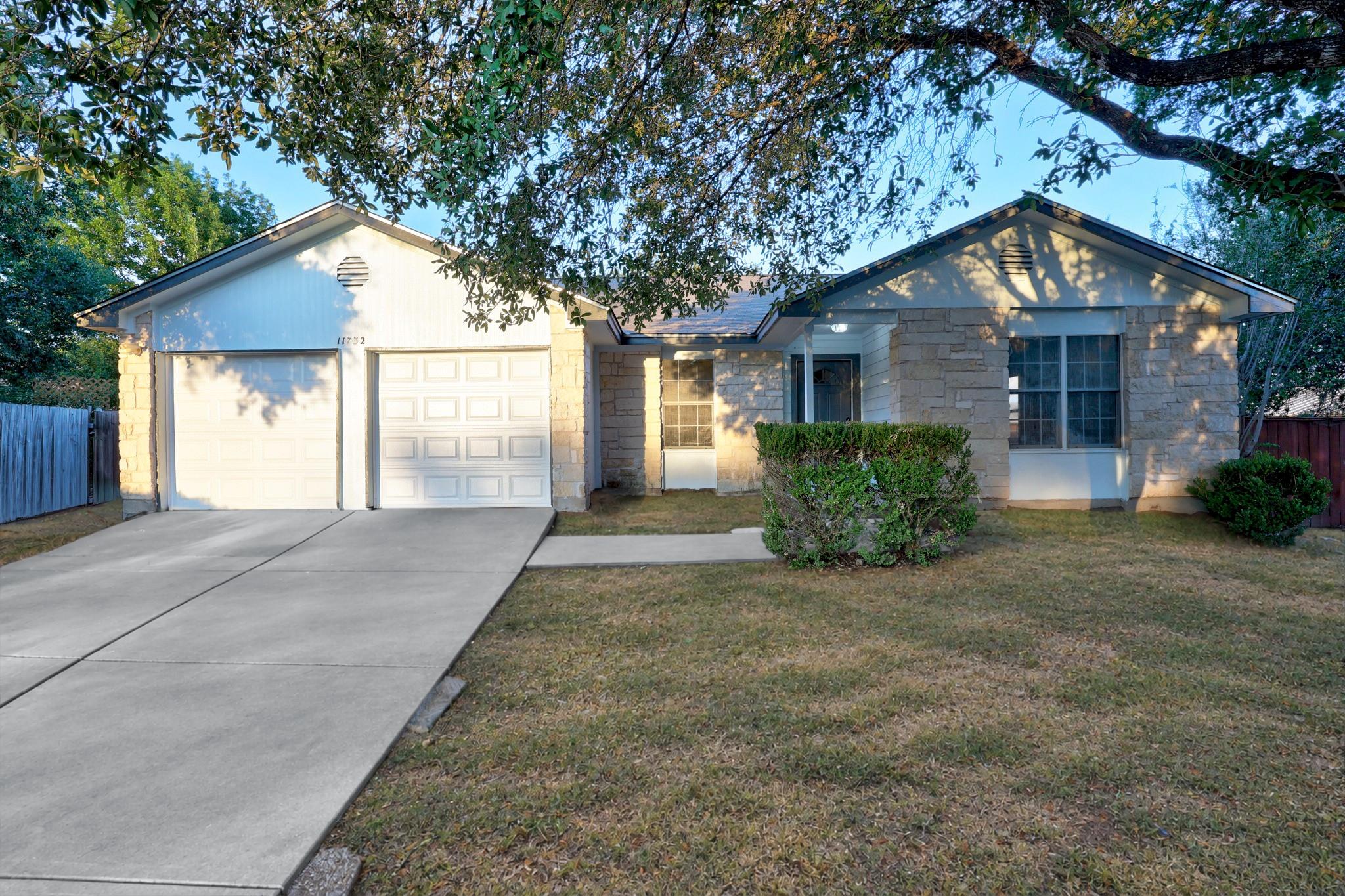 Single-story stone-front house with a two-car garage, broad driveway, and mature trees overhead.