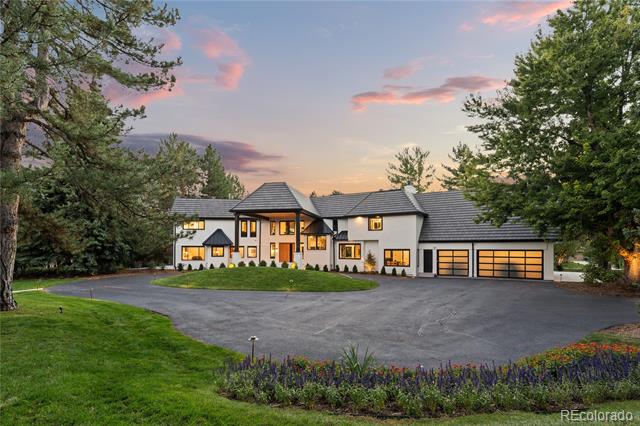 Modern white house with illuminated windows, four garage bays, and a broad curved driveway at dusk.