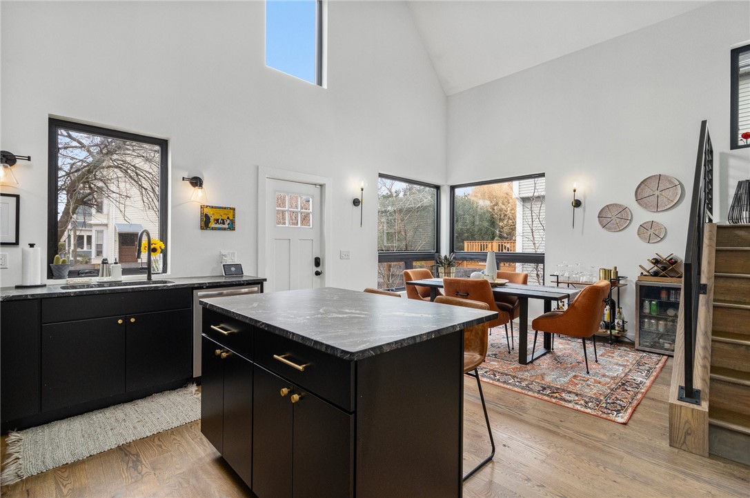Open-plan kitchen and dining area with a large black island, rust-colored chairs, and tall windows.