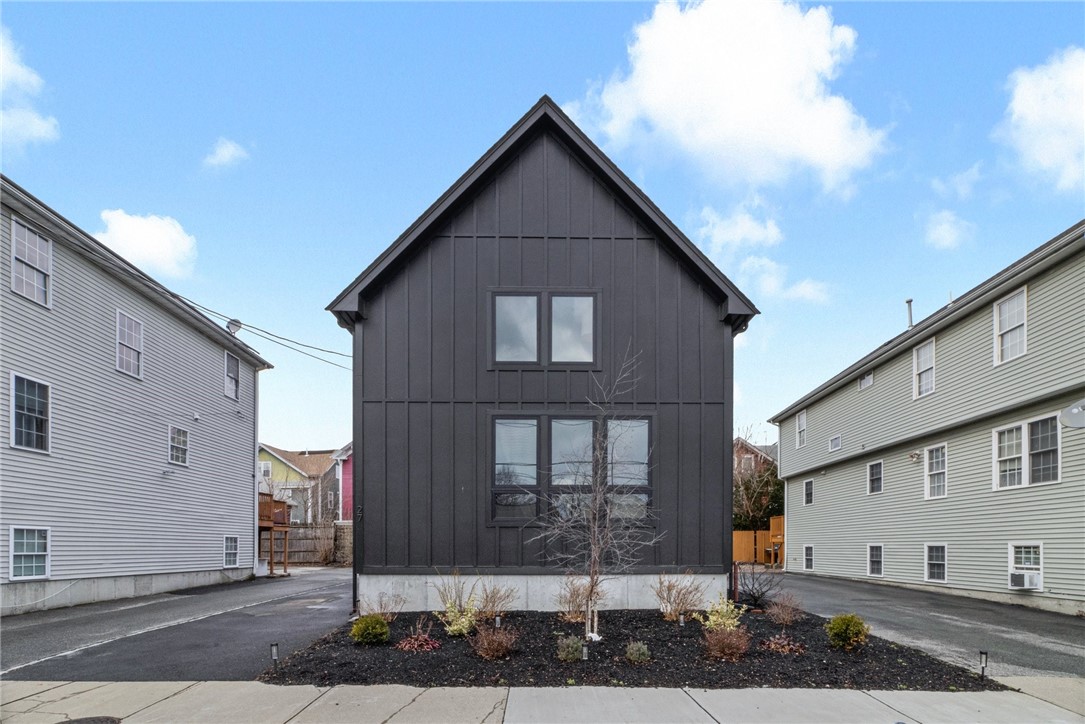 Modern dark-sided house with a steep gabled roof and landscaped front bed.