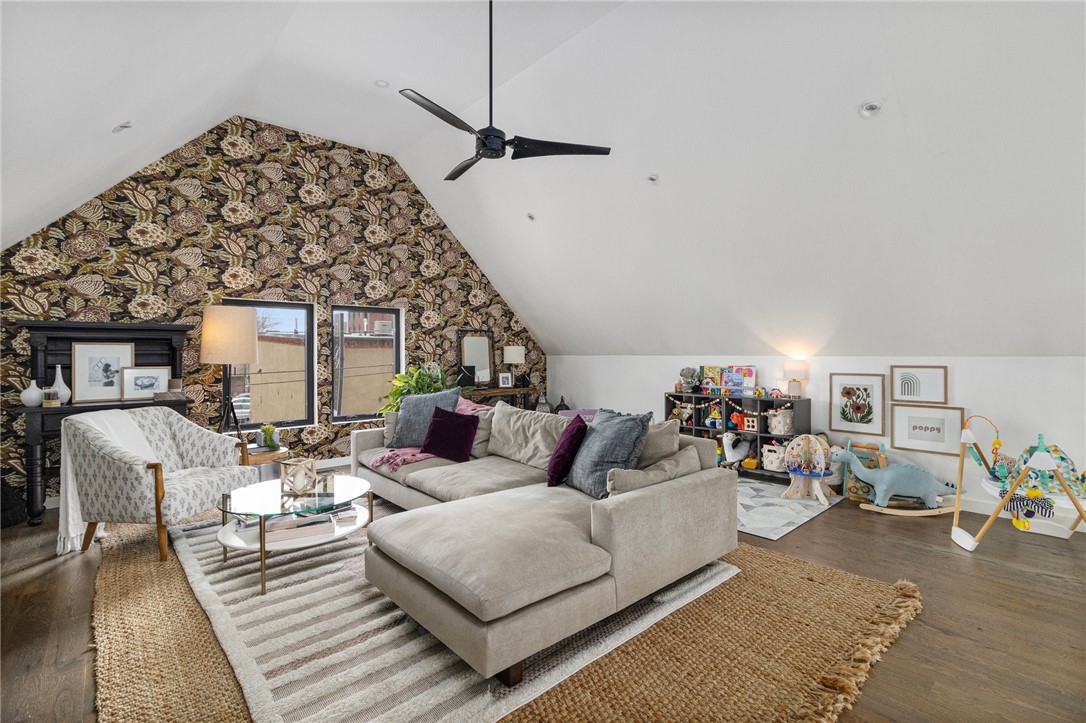 Living room with a beige sectional, floral wallpaper accent wall, vaulted ceiling, and children's play area.