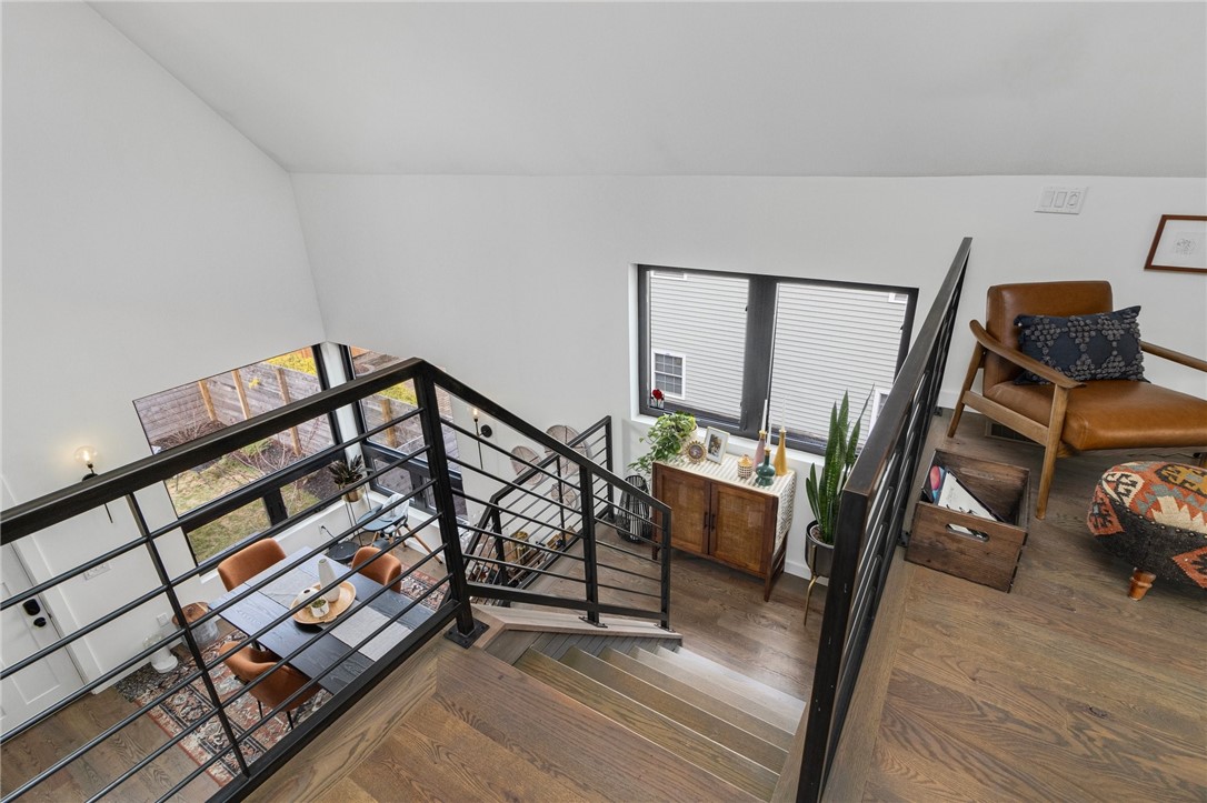 Open staircase with black metal railings overlooks a furnished living and dining area.