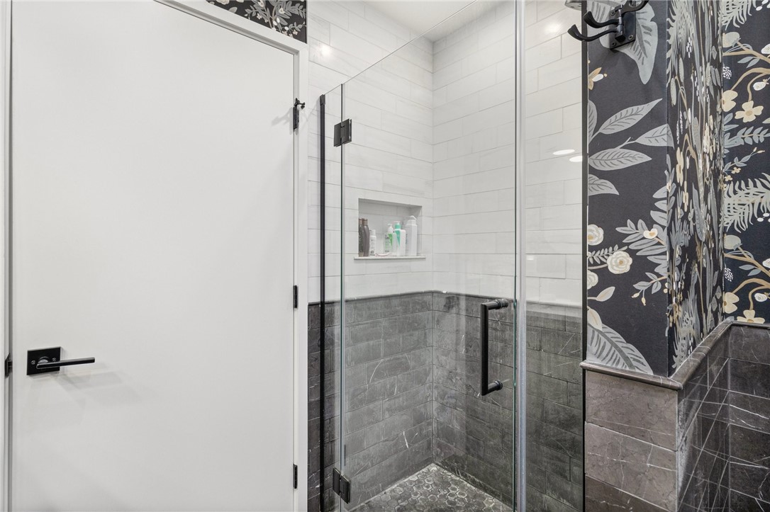 Bathroom with a glass-enclosed tiled shower, recessed niche, and dark floral wallpaper.