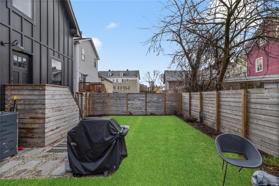 Fenced backyard with a green lawn, covered grill, and outdoor chair.