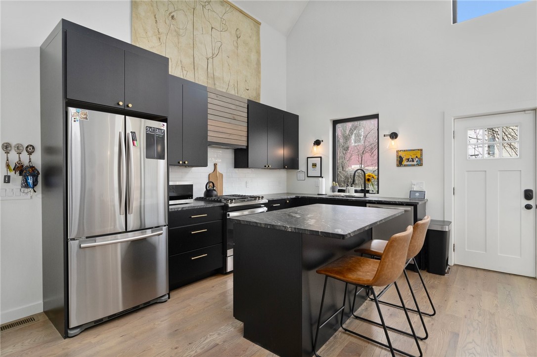 Modern kitchen with black cabinets, stainless-steel appliances, and a large island with two stools.
