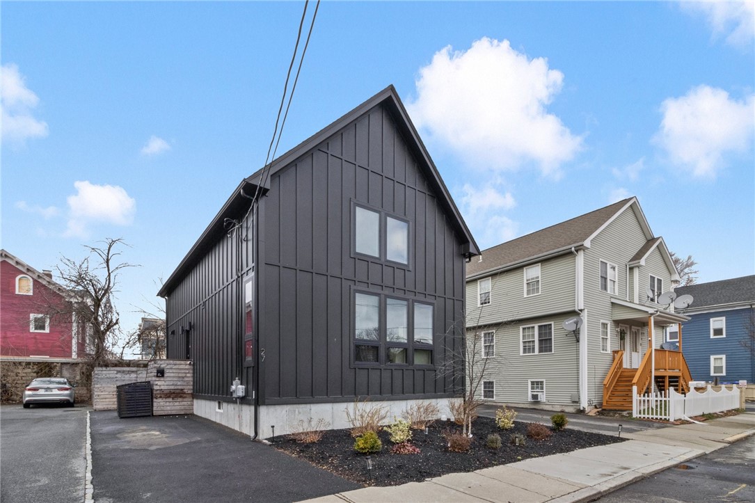 Modern charcoal-gray home with a steep gable roof, large windows, and a small landscaped front yard.