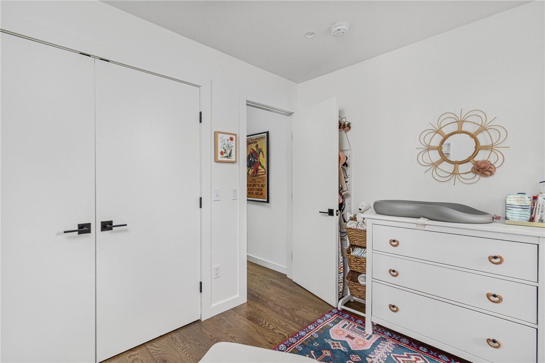 Bedroom with white closet doors, a dresser and changing pad, woven baskets, and a colorful rug.