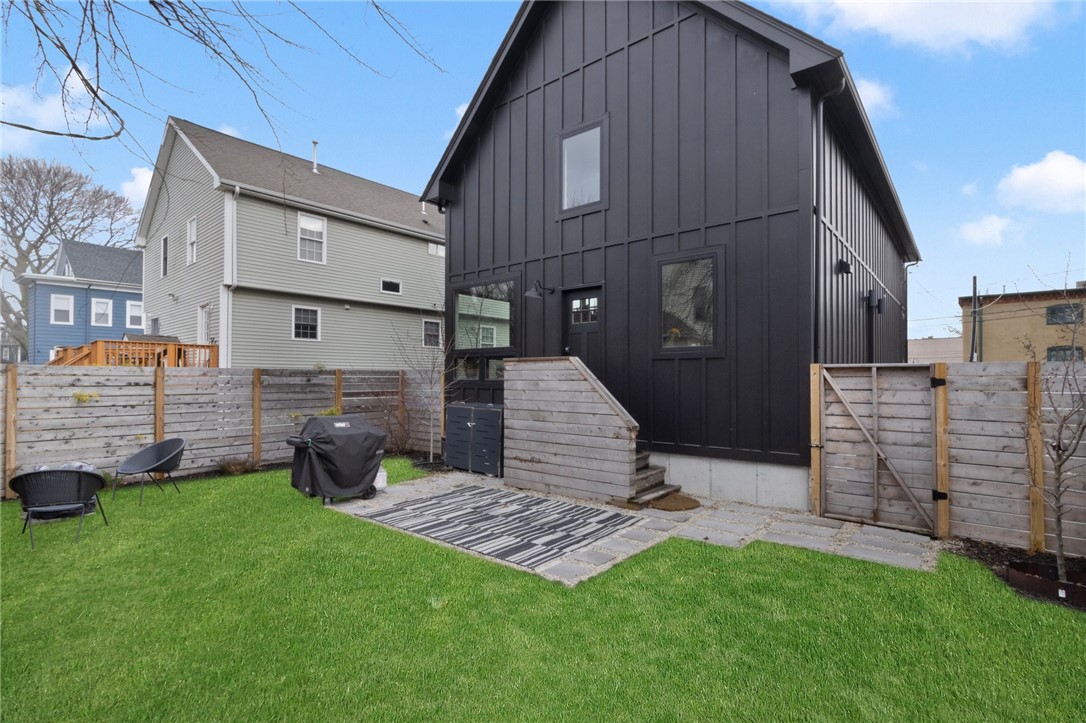 Dark barn-style house behind a fenced lawn with patio seating and a covered grill.