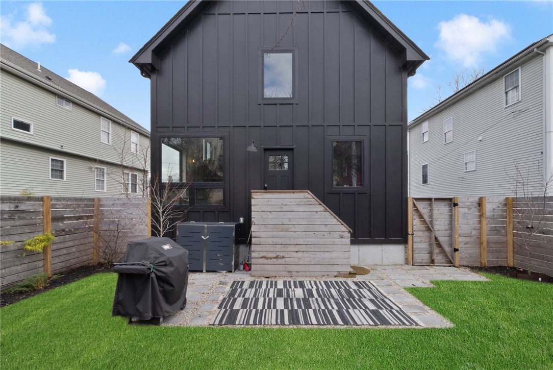 Rear of a dark charcoal house with a fenced lawn, stone patio, and covered grill.