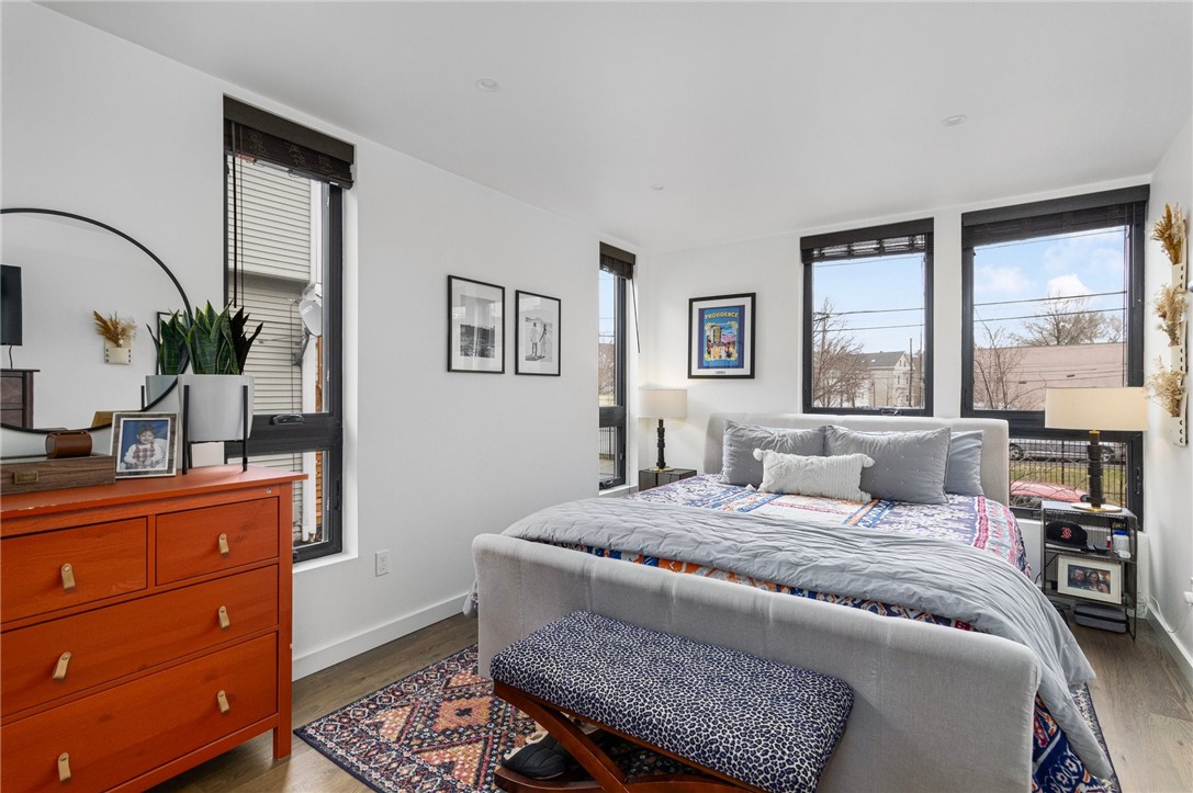 Furnished bedroom with a gray bed, colorful patterned bedding, tall black-framed windows, and an orange dresser.