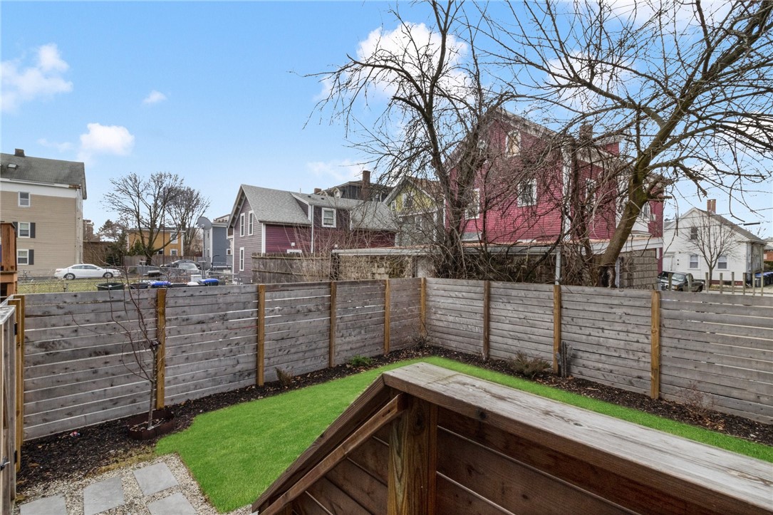 Fenced backyard with a green lawn, wooden privacy fence, and raised deck beside neighboring houses.