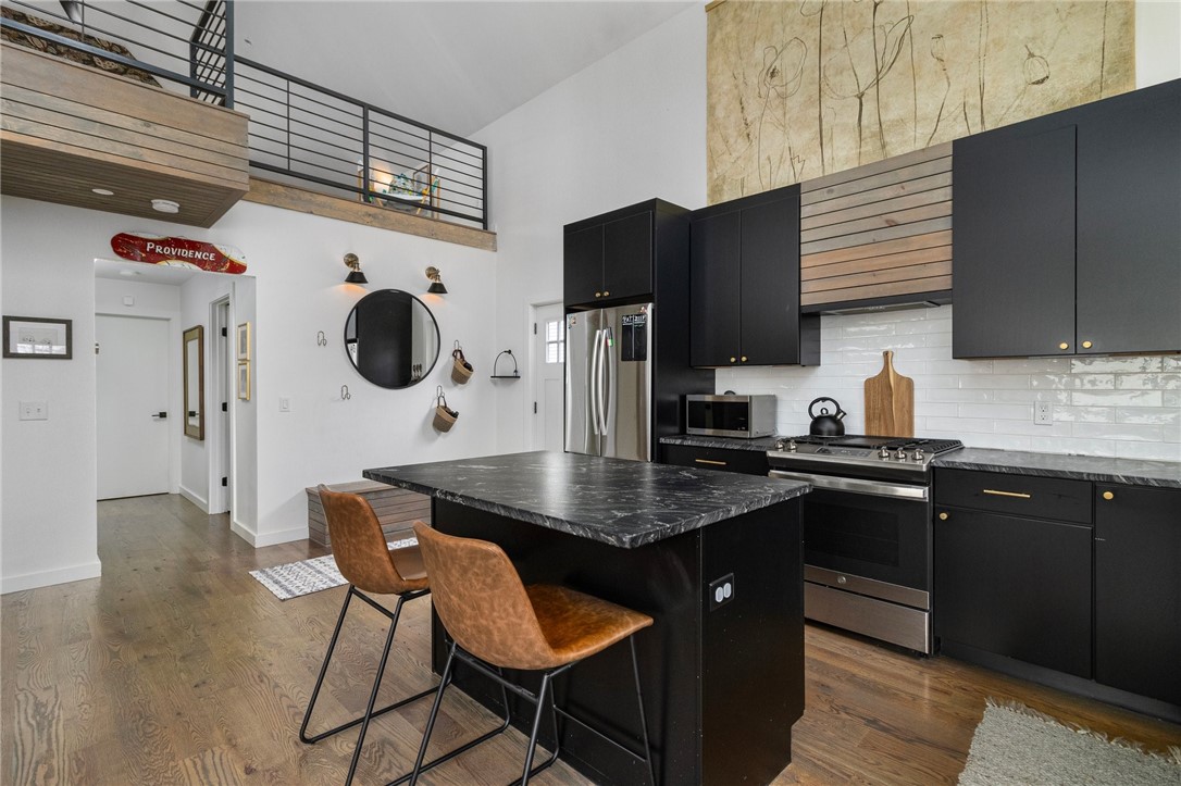 Open kitchen with black cabinets, a large stone island, and two brown leather chairs.