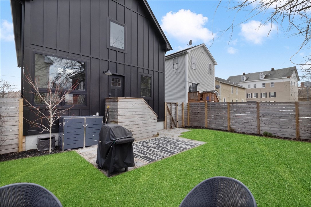 Backyard with a green lawn, black house exterior, wooden deck, privacy fence, and covered grill.