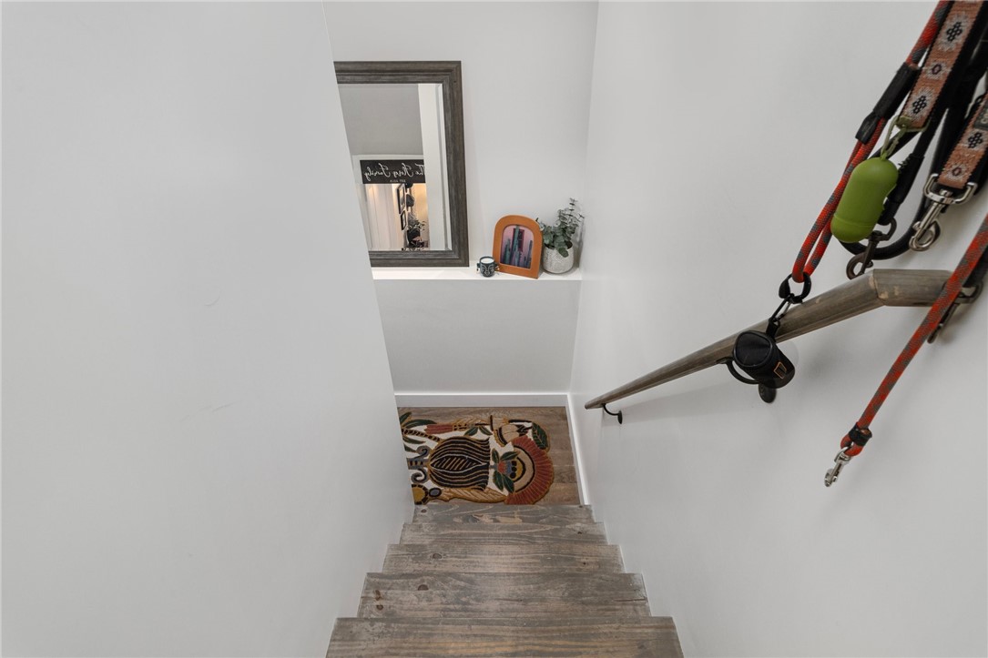 Narrow staircase with weathered wooden steps, a wall handrail, and a patterned rug on the landing.