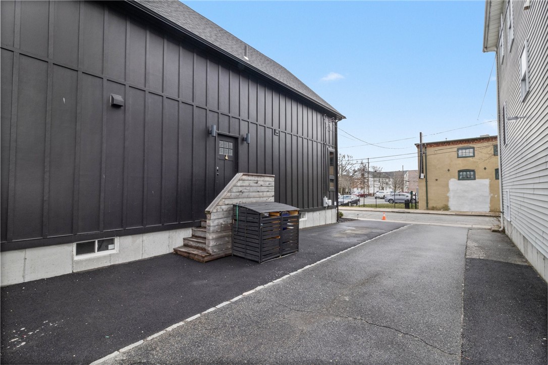 Black-sided building beside a paved driveway, with wooden steps leading to a raised entrance.