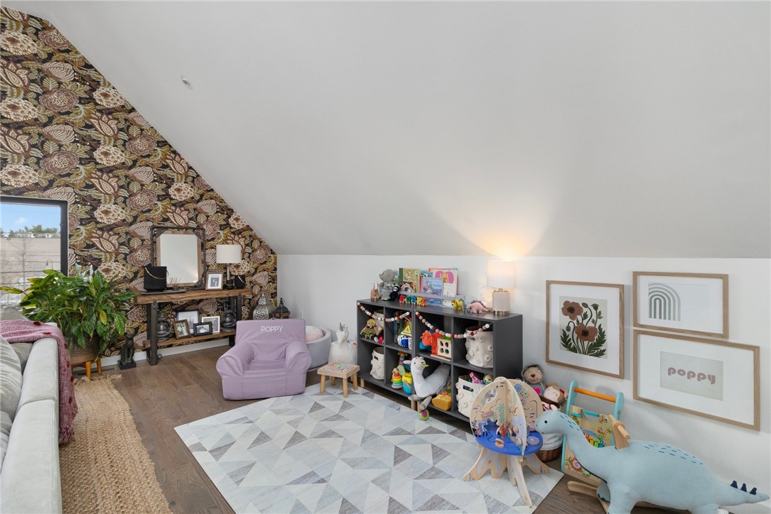 Attic playroom with floral wallpaper, a lavender child-sized chair, toy shelves, and a geometric rug.