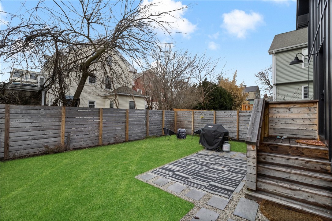 Fenced backyard with a green lawn, stone patio, and raised wooden deck.