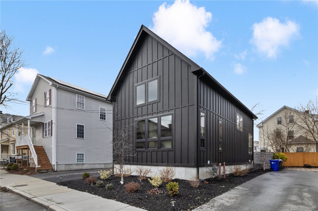 Modern dark-sided gabled home with tall windows and a landscaped yard beside the driveway.