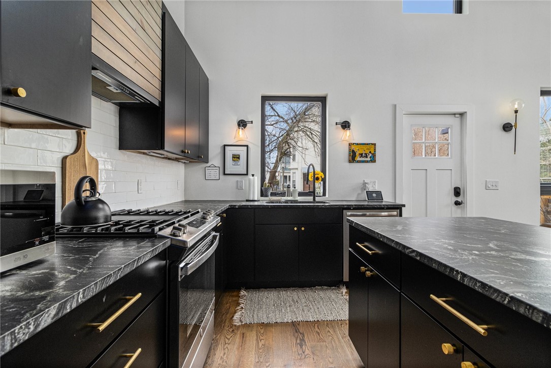 Modern kitchen with black cabinetry, veined stone counters, a large island, and stainless steel range.