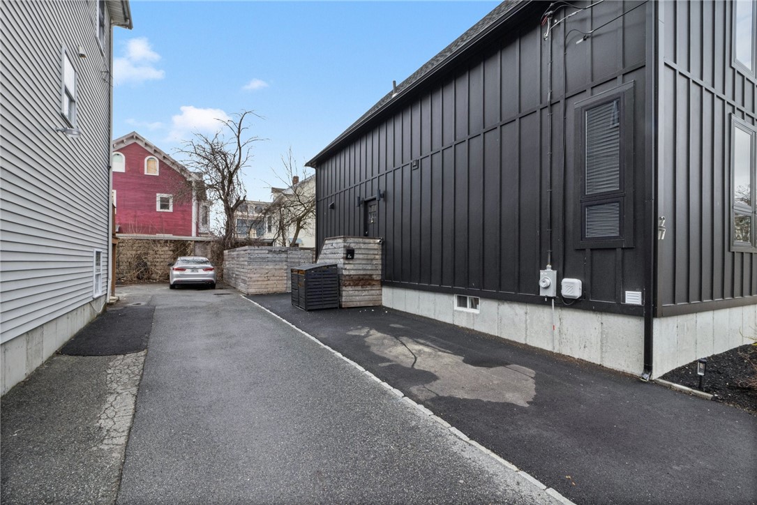 Dark metal-sided building beside a narrow driveway and wooden enclosure.