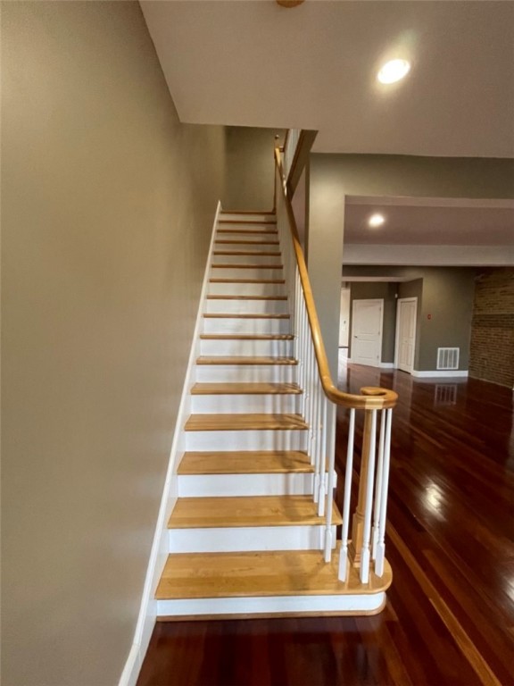 Wood-and-white staircase with a curved handrail beside a spacious room with polished hardwood floors.