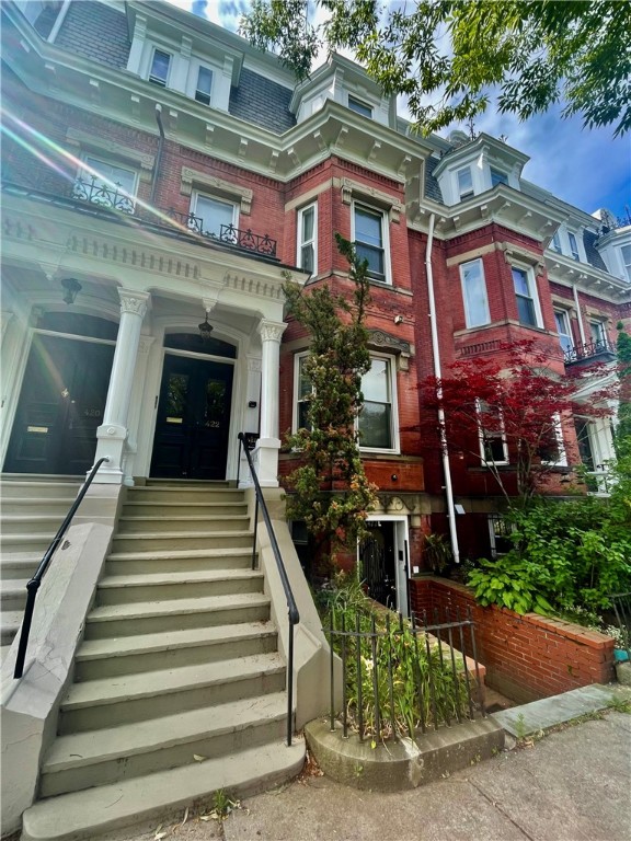 Red-brick residence with ornate white trim, a broad front stoop, and a planted garden.