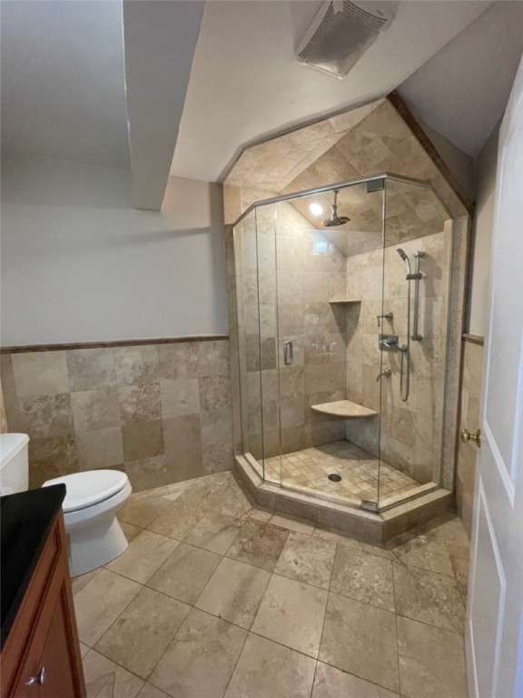 Tiled bathroom with a glass corner shower, built-in bench, toilet, and partially visible wood vanity.