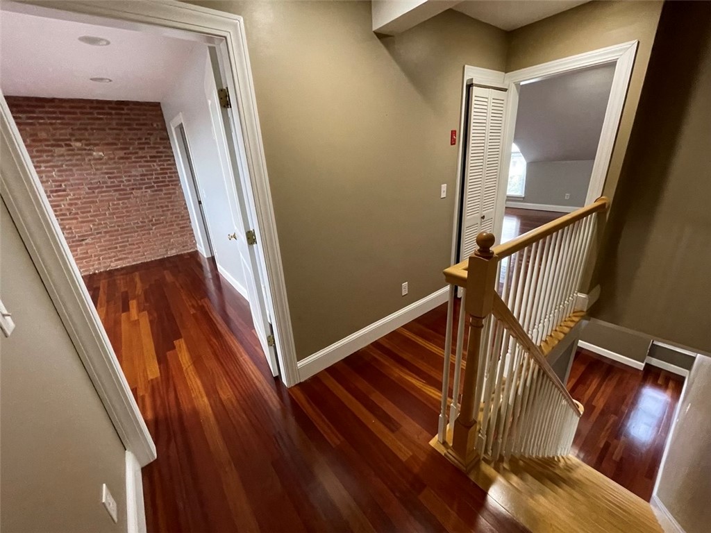 Hallway and stair landing with polished hardwood floors, white balusters, and an exposed brick wall through a doorway.