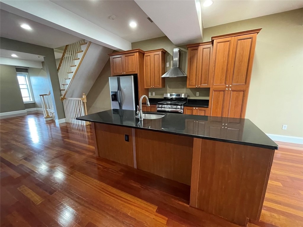 Kitchen with a large dark island, warm wood cabinetry, stainless steel appliances, and hardwood floors.
