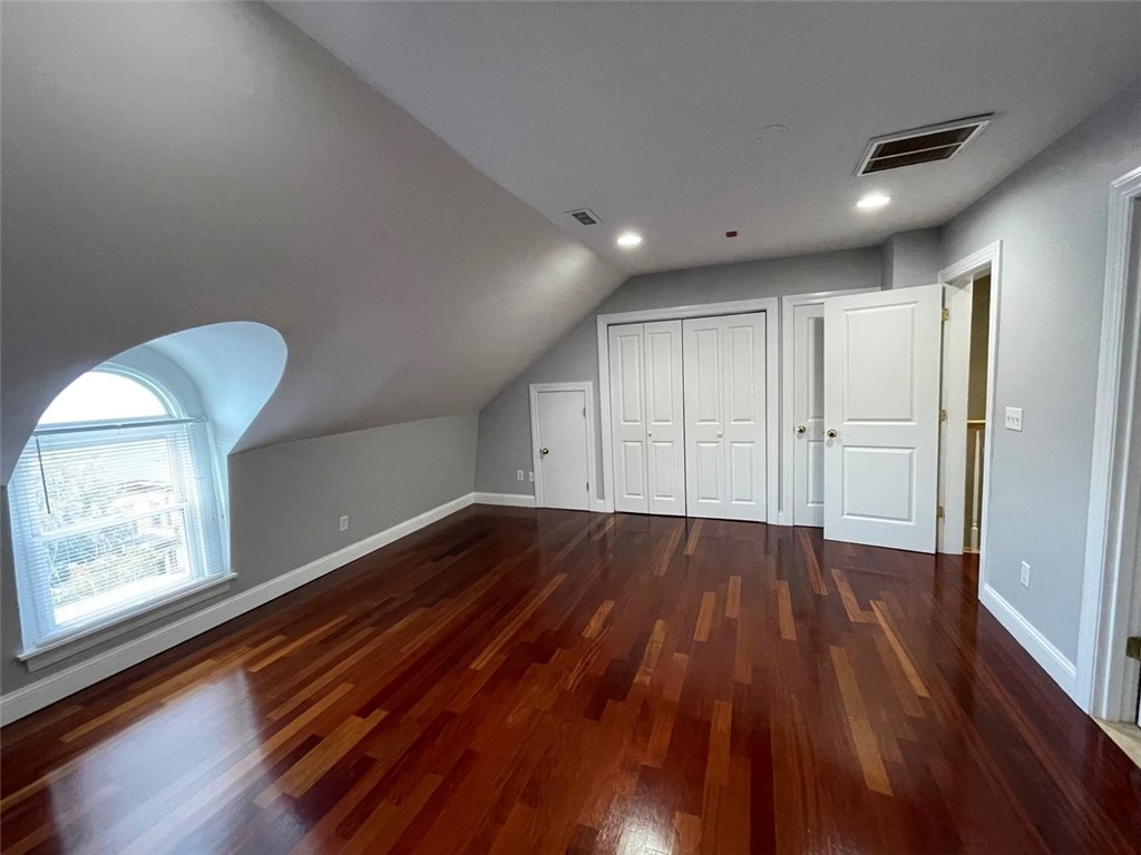 Empty upper-floor room with polished hardwood floors, a sloped ceiling, and an arched window.