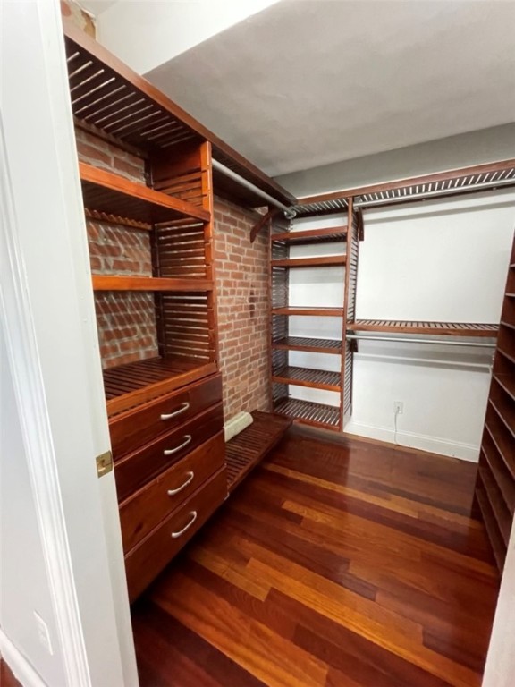 Walk-in closet with reddish wood shelving, drawers, exposed brick, and hardwood flooring.