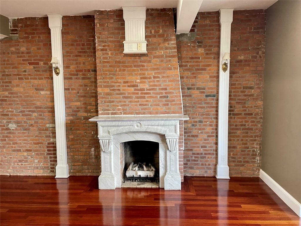 Room with a marble fireplace set against an exposed brick wall and polished hardwood floors.