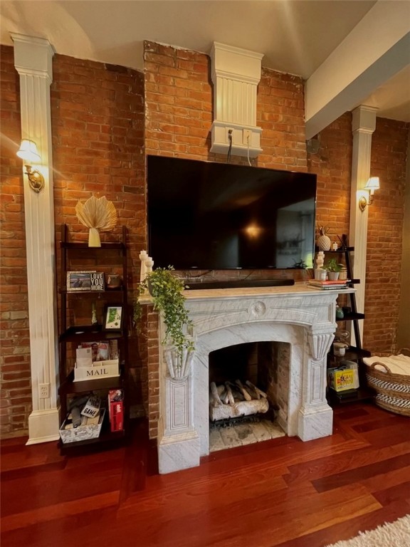 Living room with a carved white fireplace, exposed brick walls, and a large TV above the mantel.