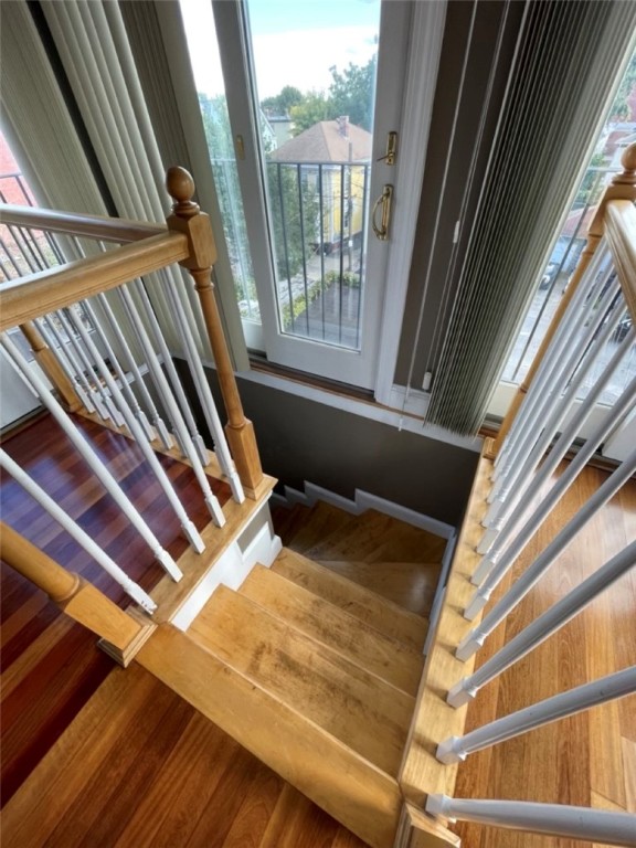Wooden staircase with white balusters leading down from a landing beside a glass balcony door.