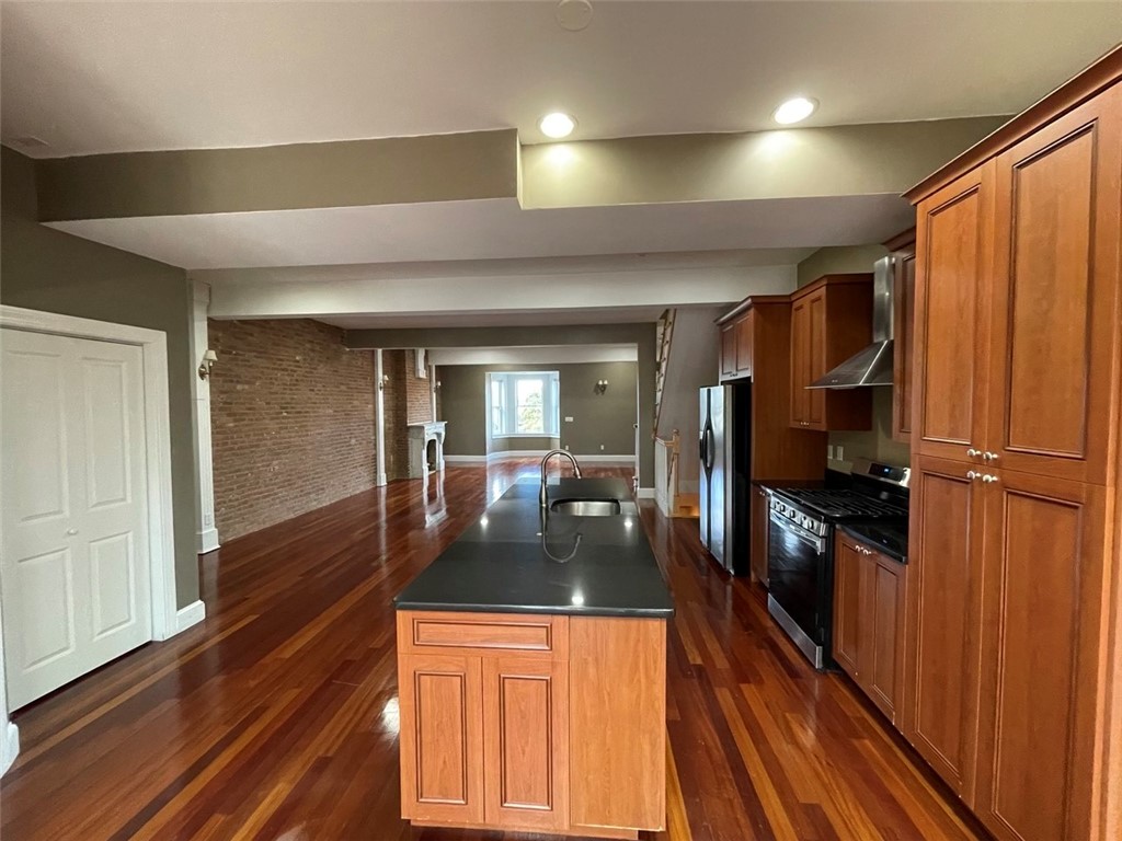 Open-plan kitchen with a wood-cabinet island, stainless steel appliances, and exposed brick wall.