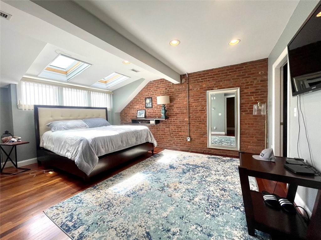 Bedroom with exposed brick walls, two skylights, a large bed, and a blue patterned rug.