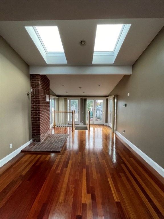 Empty living room with polished hardwood floors, a brick hearth, and two skylights.