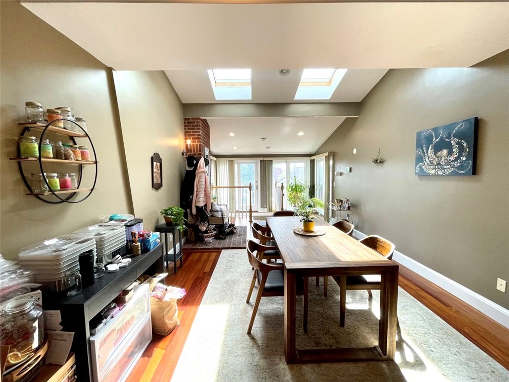 Dining room with a long wooden table, hardwood floors, skylights, and large windows.