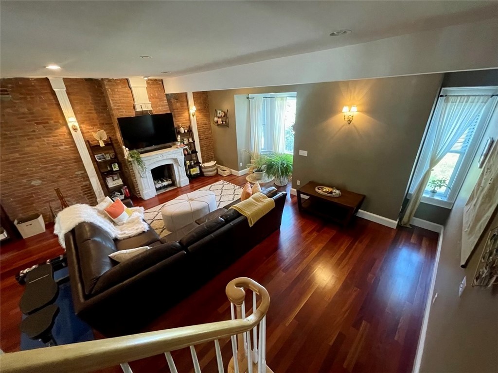 Living room with exposed brick, white fireplace, leather sectional, and polished hardwood floors.