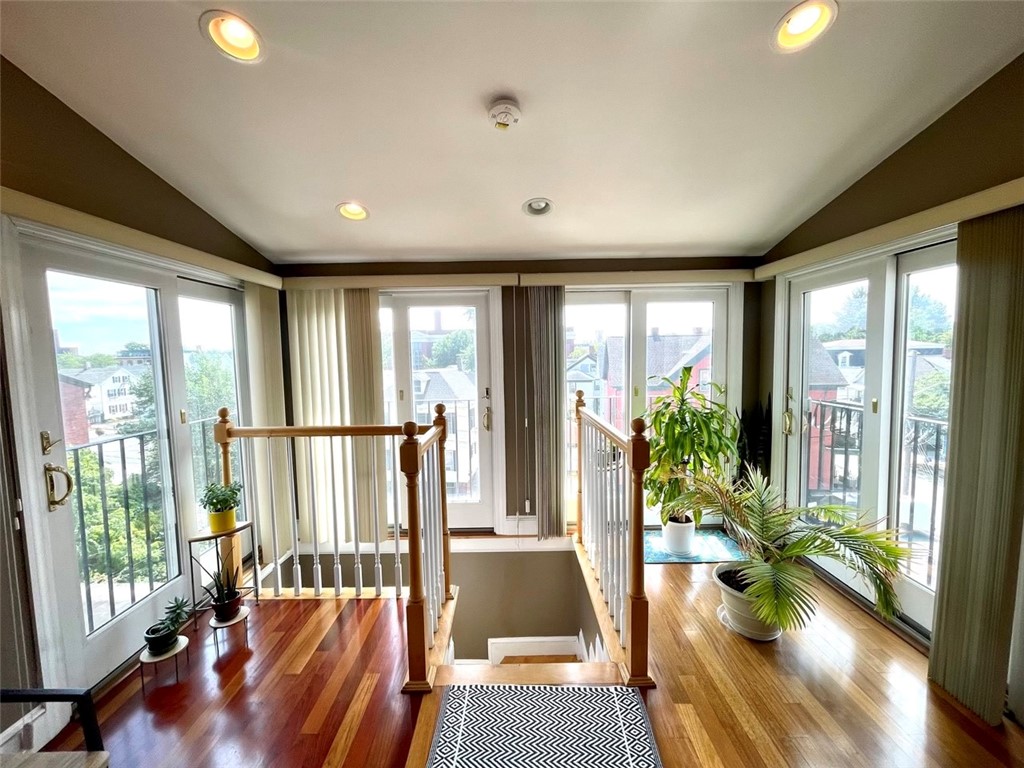 Bright stair landing with polished wood floors, tall windows, and potted plants.