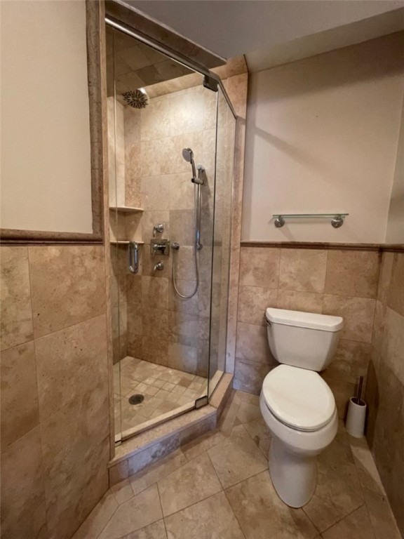 Bathroom with a glass-enclosed shower, beige stone tile, and white toilet.
