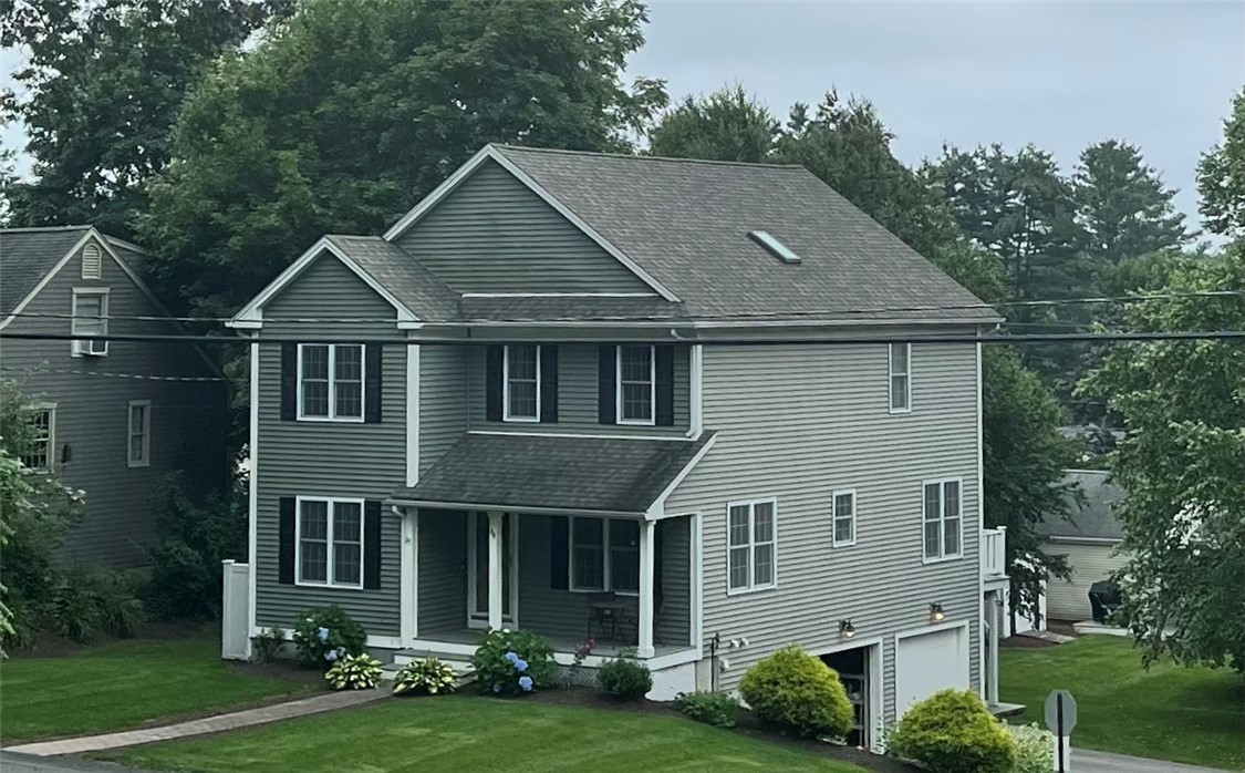 Two-story gray-sided home with a covered porch, attached garage, and landscaped lawn.
